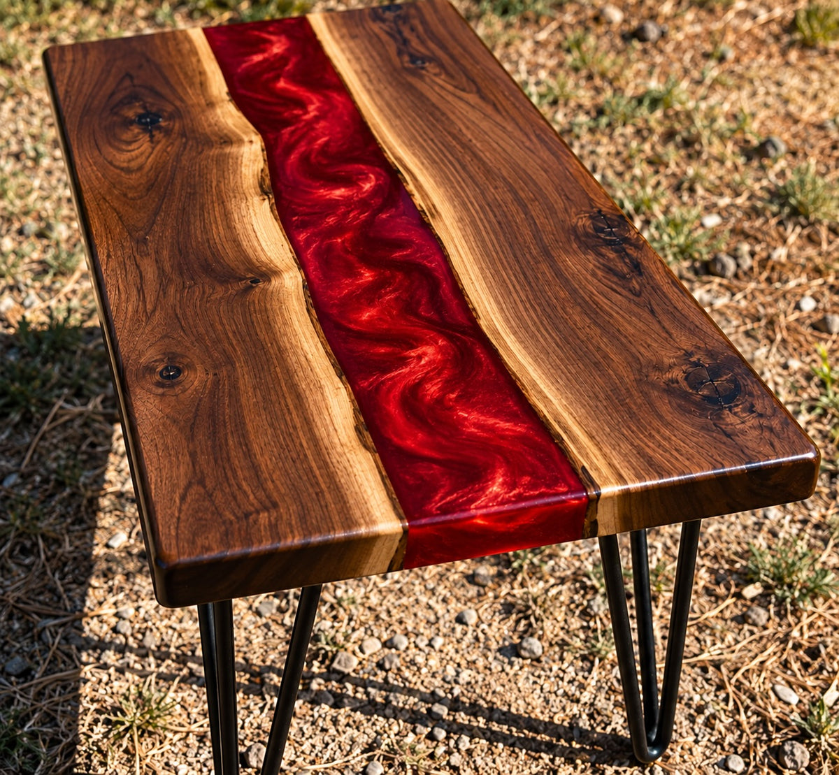 Handmade walnut epoxy river accent table with swirling ruby-red resin center, natural walnut wood grain, and black metal hairpin legs.