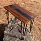 Angled view of a handmade walnut epoxy river accent table featuring a black resin river, natural walnut wood grain, and black metal hairpin legs.