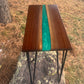 Handmade walnut epoxy river accent table with shimmering emerald-green resin center, natural walnut wood grain, and black metal hairpin legs.