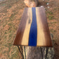 Top view of a handmade walnut epoxy river accent table with deep blue resin, contrasting natural wood grain, and black metal hairpin legs.