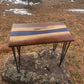 Handmade walnut epoxy river accent table featuring a blue resin center, natural walnut wood grain, and black metal hairpin legs.