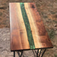 Close-up of a handmade walnut epoxy river accent table with swirling forest-green resin, natural walnut wood grain, and a polished tabletop.