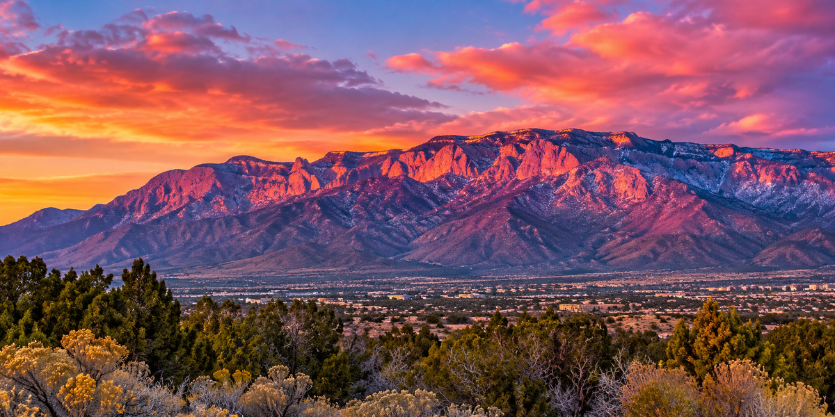 Artistic panoramic depiction of the Sandia Mountains glowing pink at sunset
